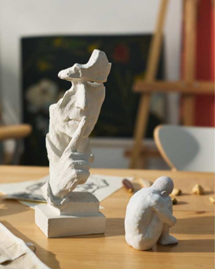 White plaster sculpture maquettes on a studio table with an easel behind, presenting proposed art solution concepts